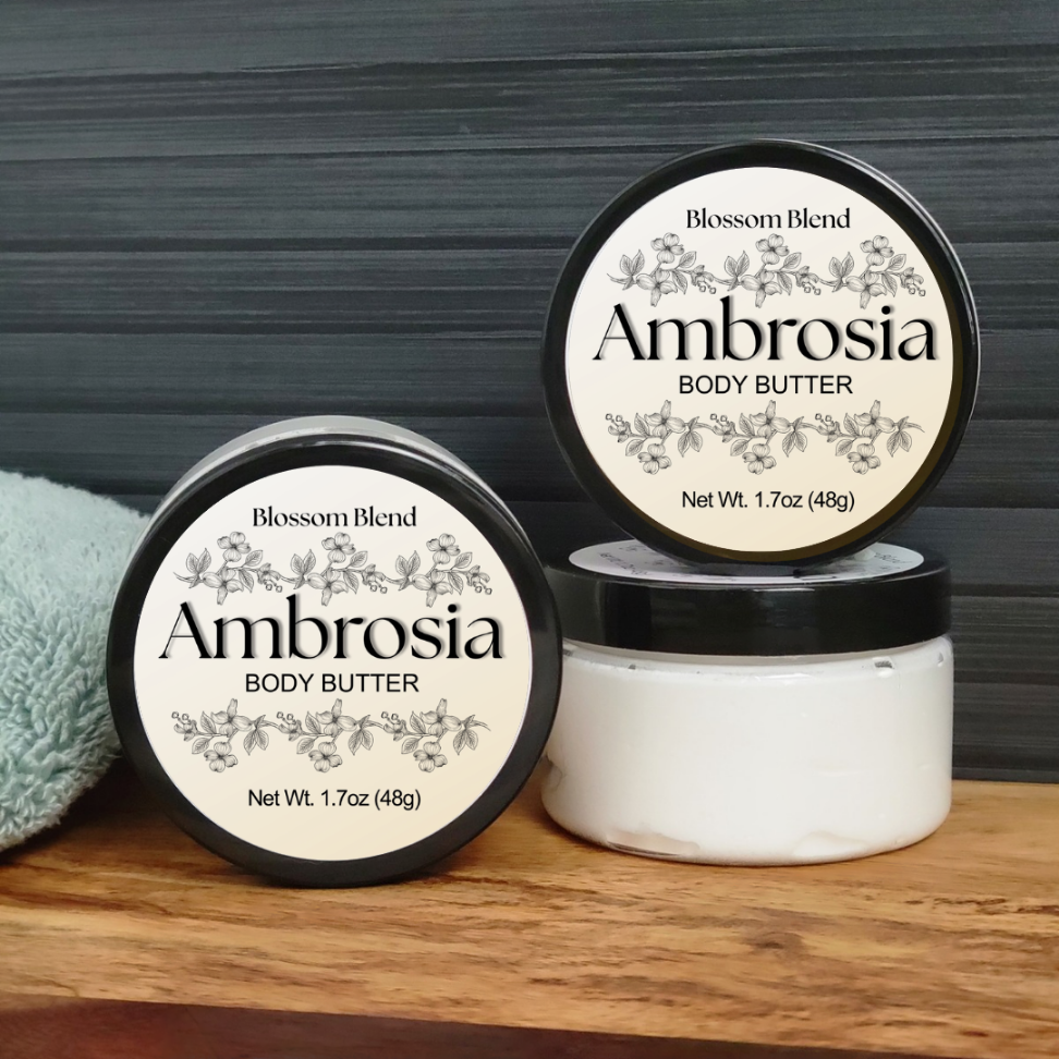 Two containers of Ambrosia body butter on a wooden surface with a gray textured background.