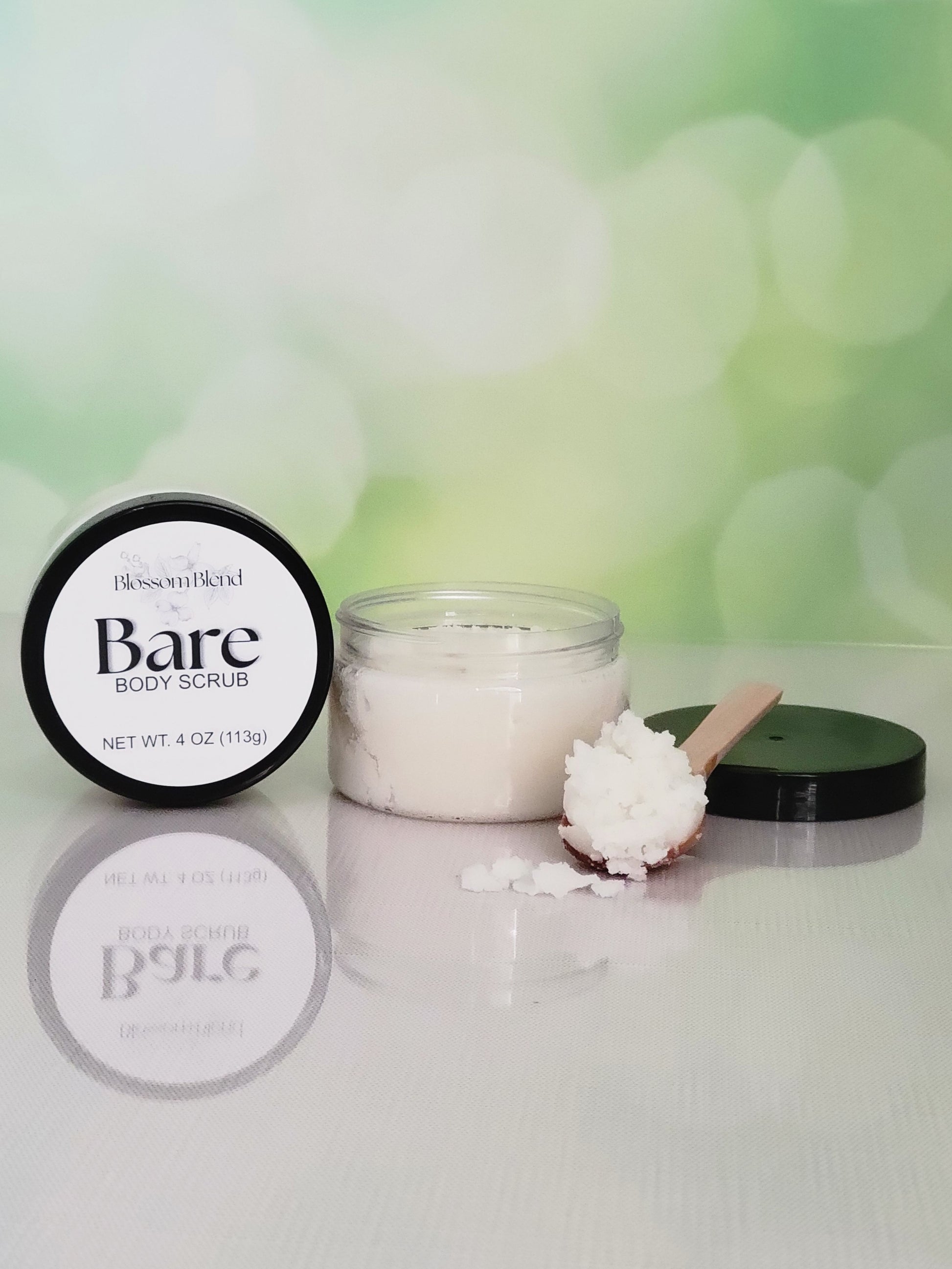 Bare Body Scrub container with a scoop of scrub on a white surface with a green blurred background