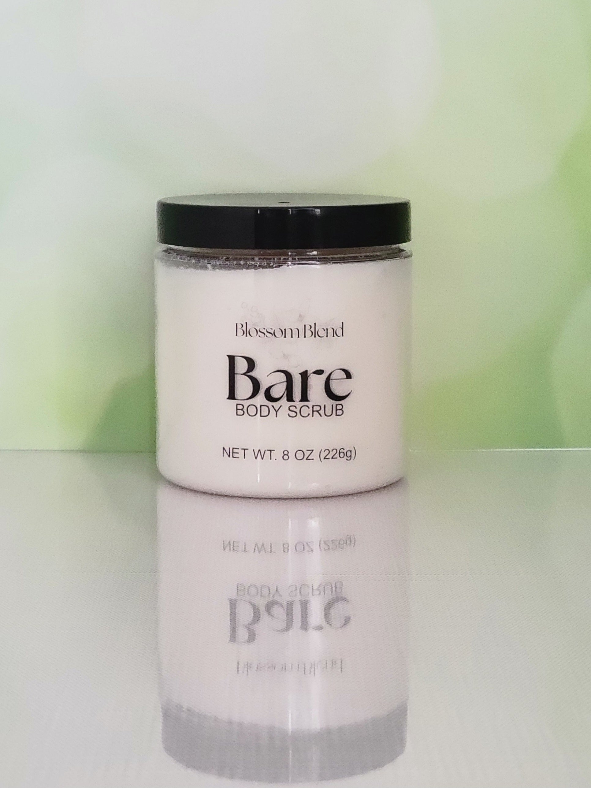 Jar of Blossom Blend Bare Body Scrub on a reflective surface with a blurred green background