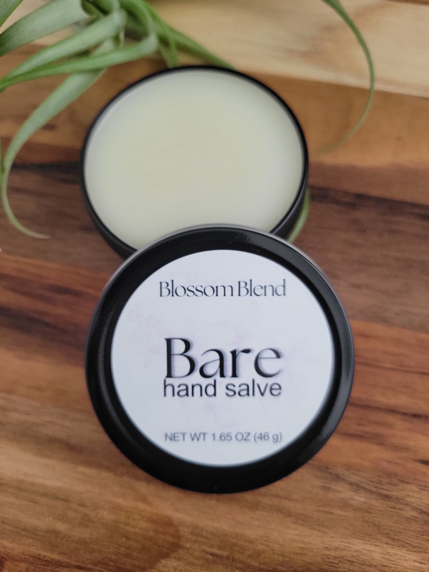 Bottle of Bare hand salve on a wooden surface with a plant in the corner