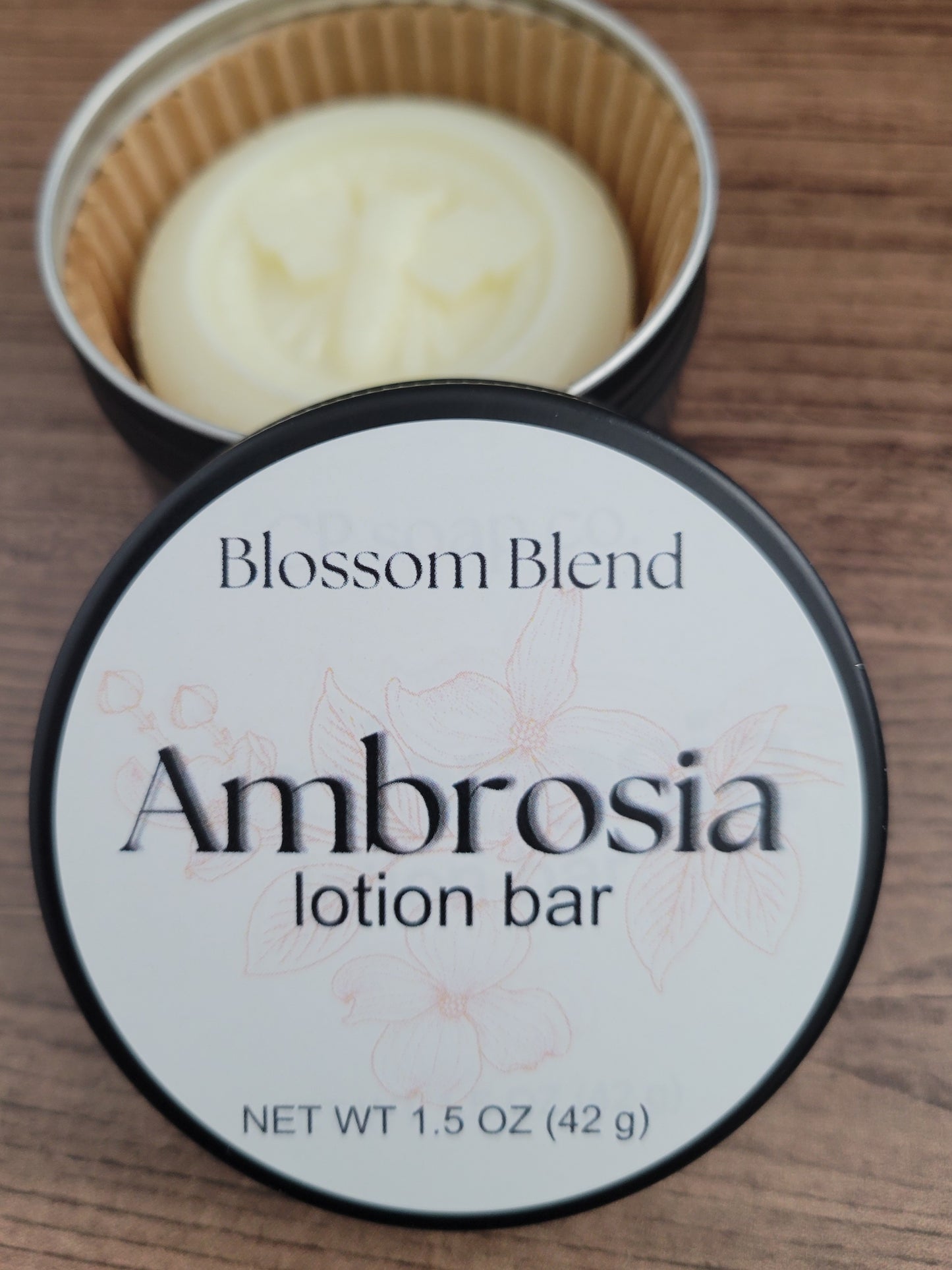 Blossom Blend Ambrosia lotion bar in a container on a wooden surface