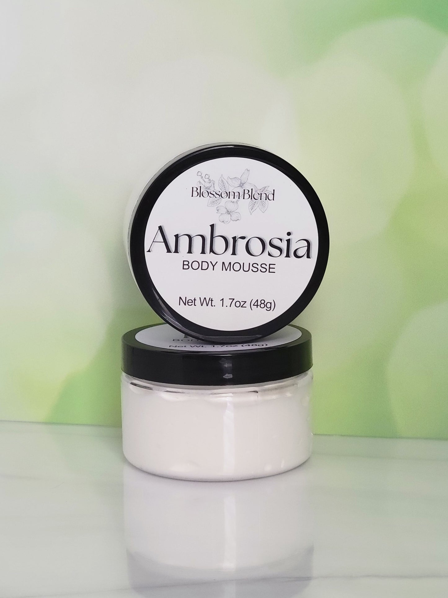 Jar of Ambrosia body mousse with a green gradient background