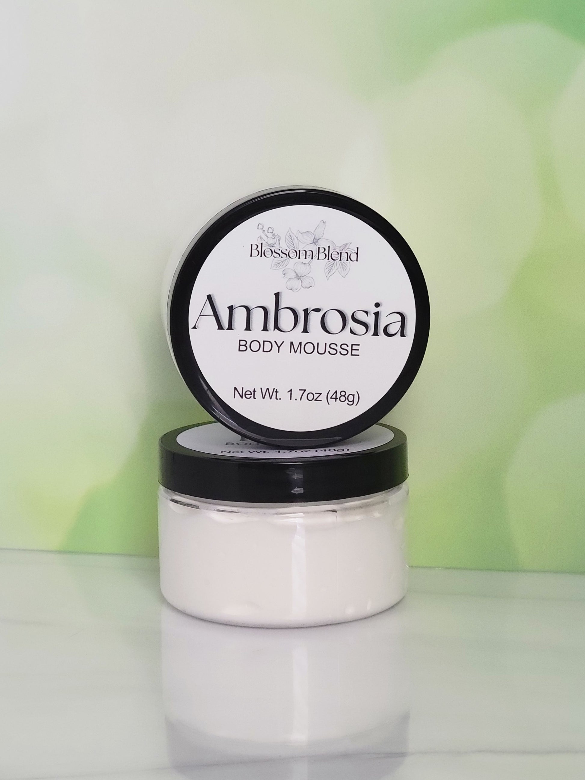 Jar of Ambrosia body mousse with a green gradient background