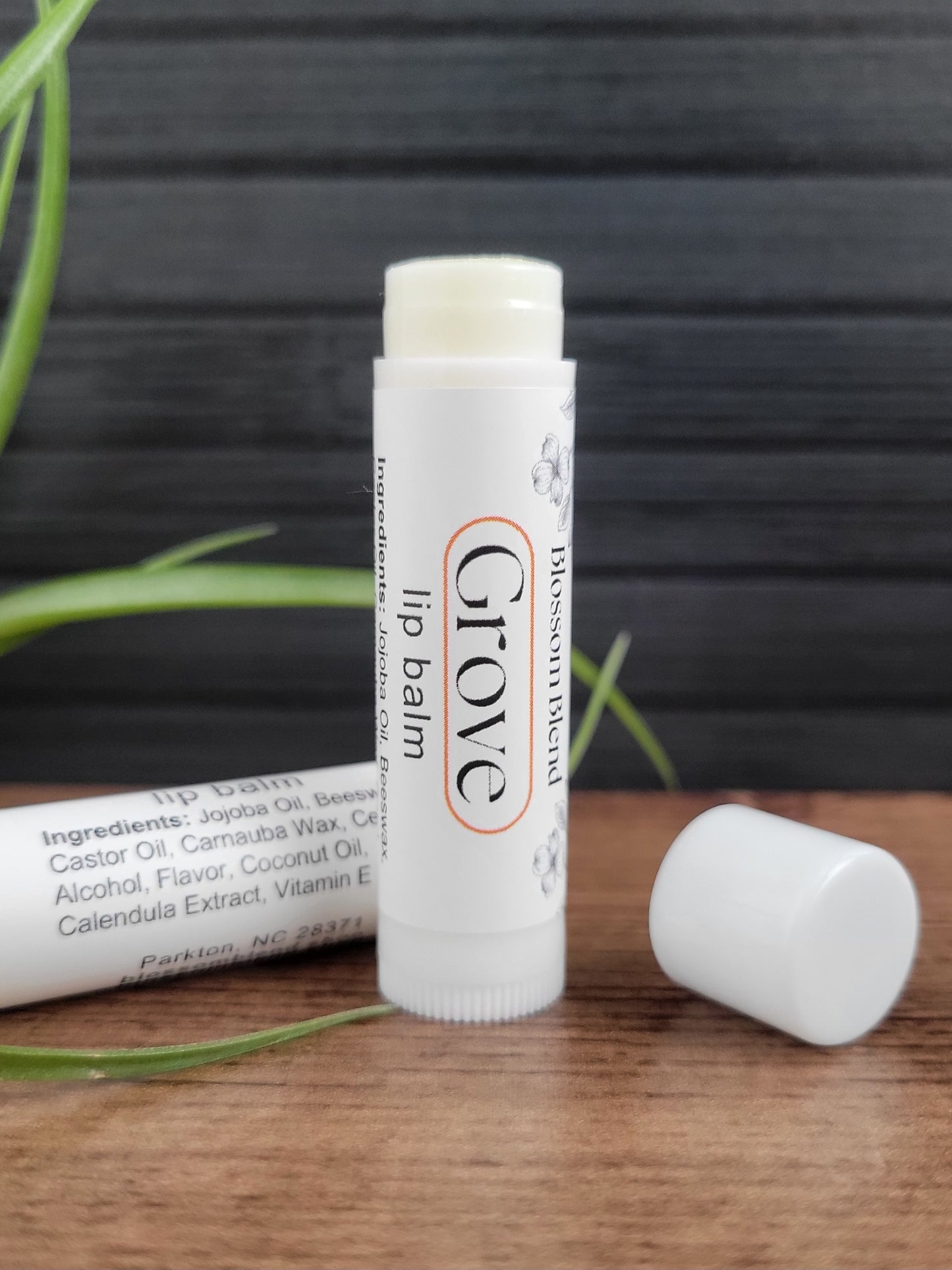 Glove lip balm on a wooden surface with a plant in the background