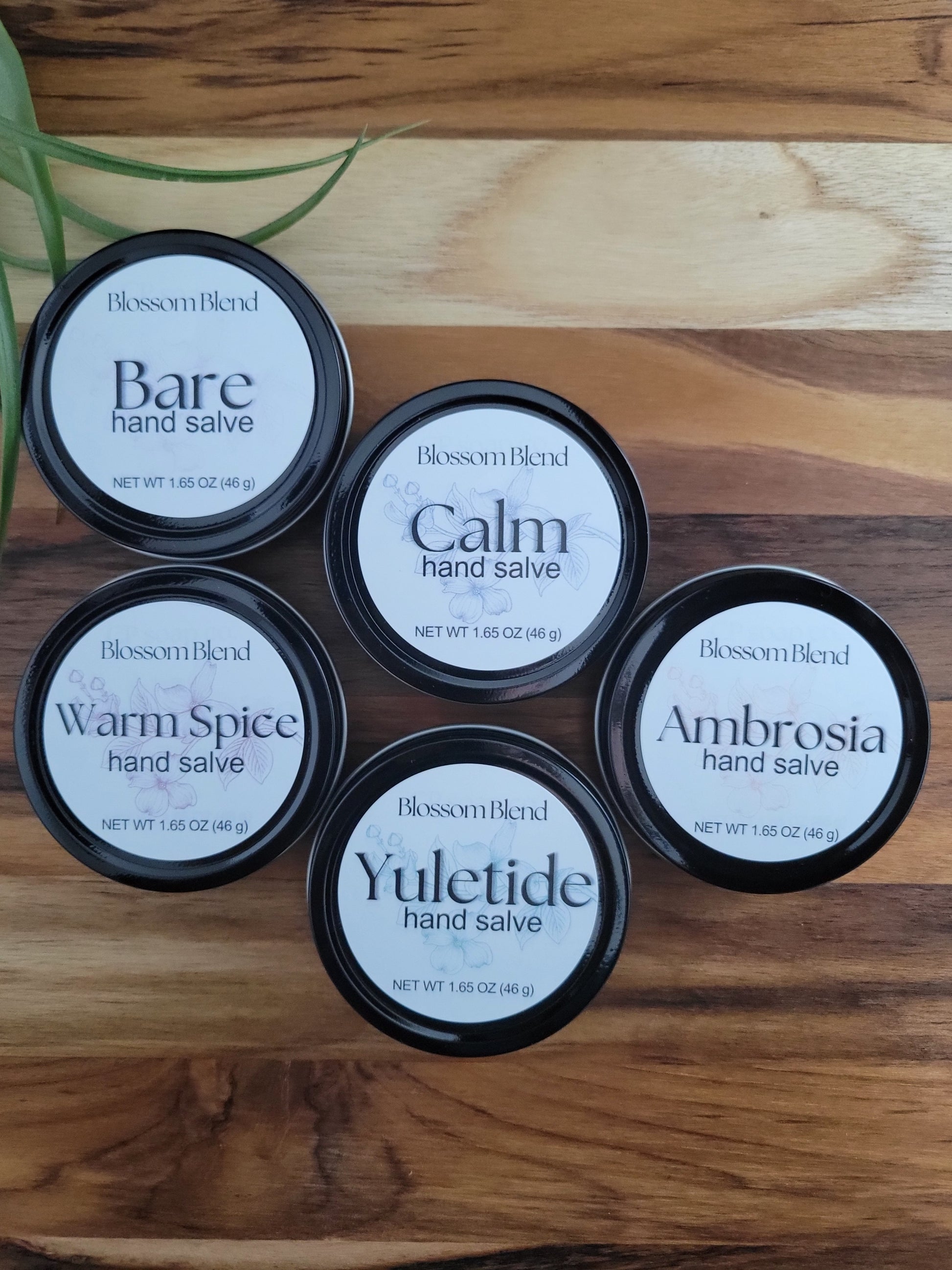 Five containers of Blossom Blend hand salves on a wooden surface