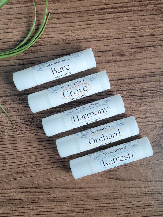 Five lip balms labeled 'Bare', 'Grove', 'Harmony', 'Orchard', and 'Refresh' on a wooden surface.
