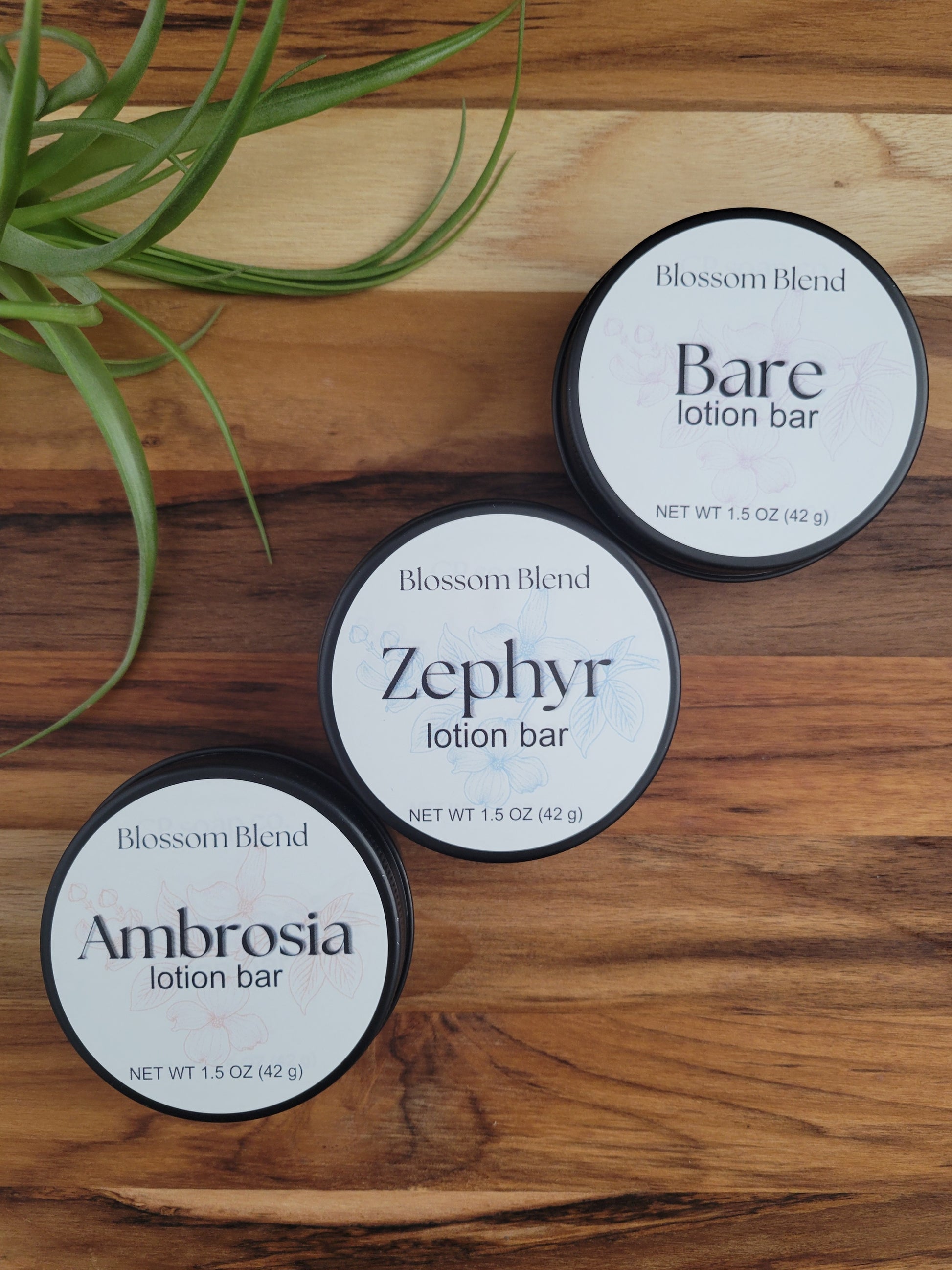 Three Blossom Blend lotion bars on a wooden surface with a plant.