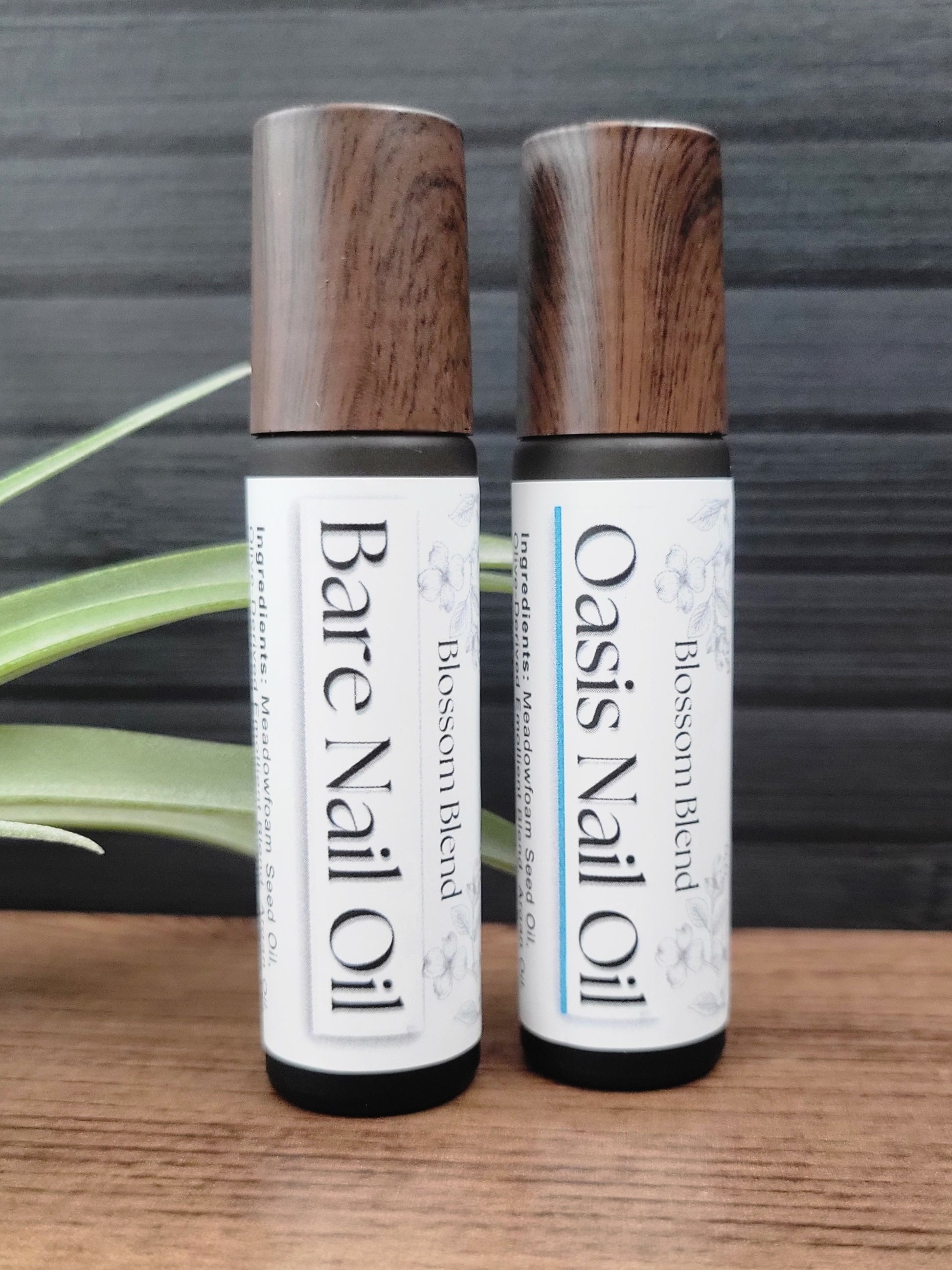 Two bottles of Bare Nail Oil and Oasis Nail Oil on a wooden surface with a natural background.