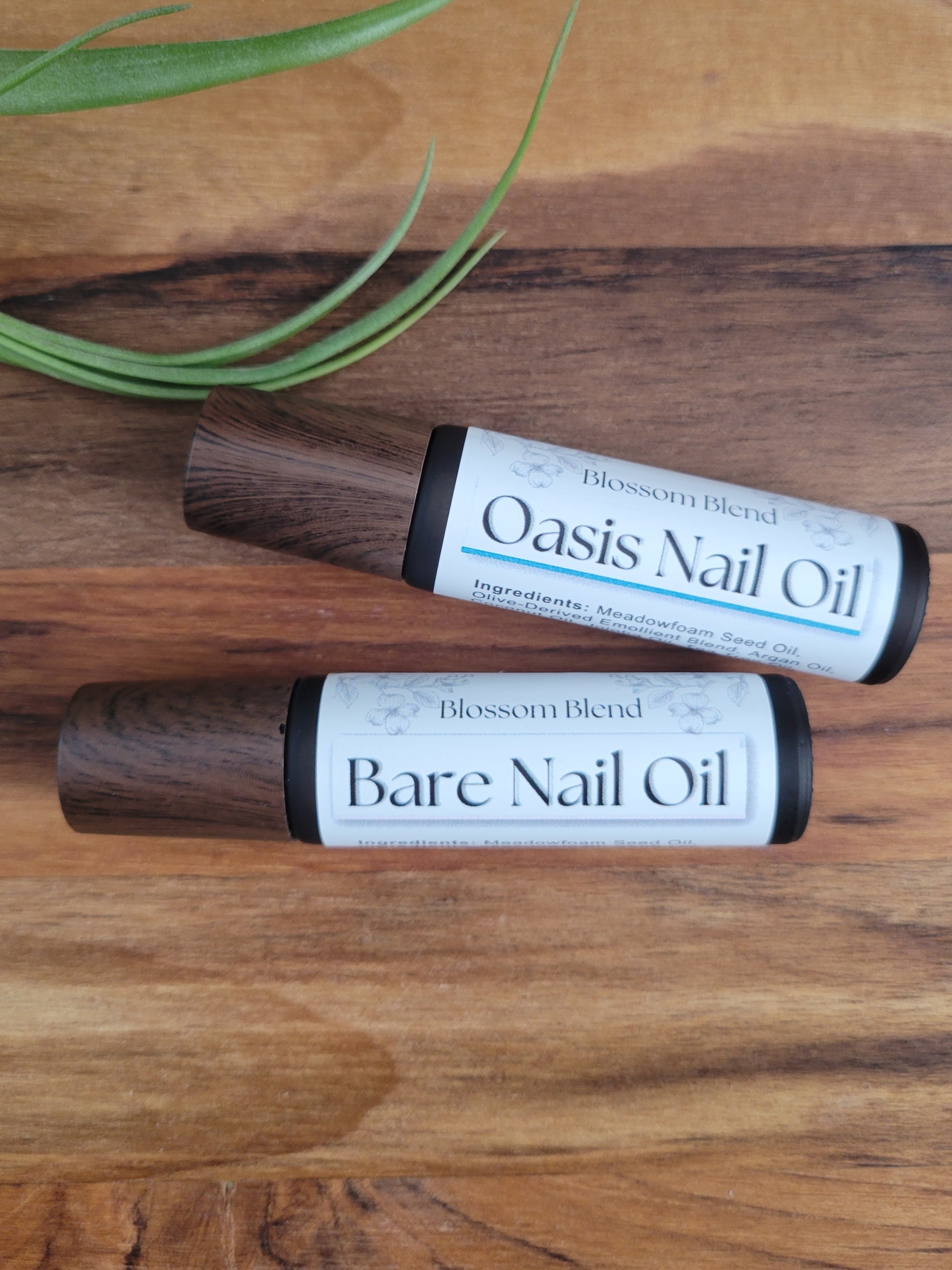 Two bottles of Blossom Blend nail oil on a wooden surface with a plant leaf.