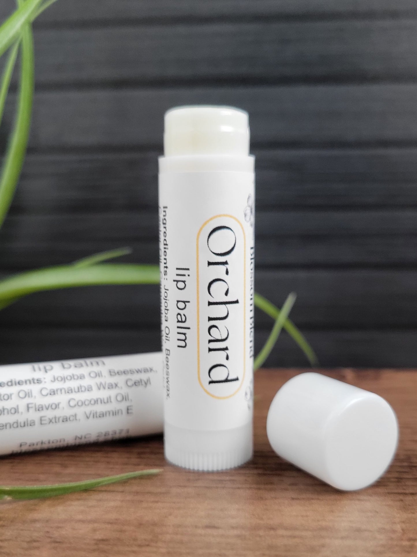 Orchard lip balm on a wooden surface with a dark background
