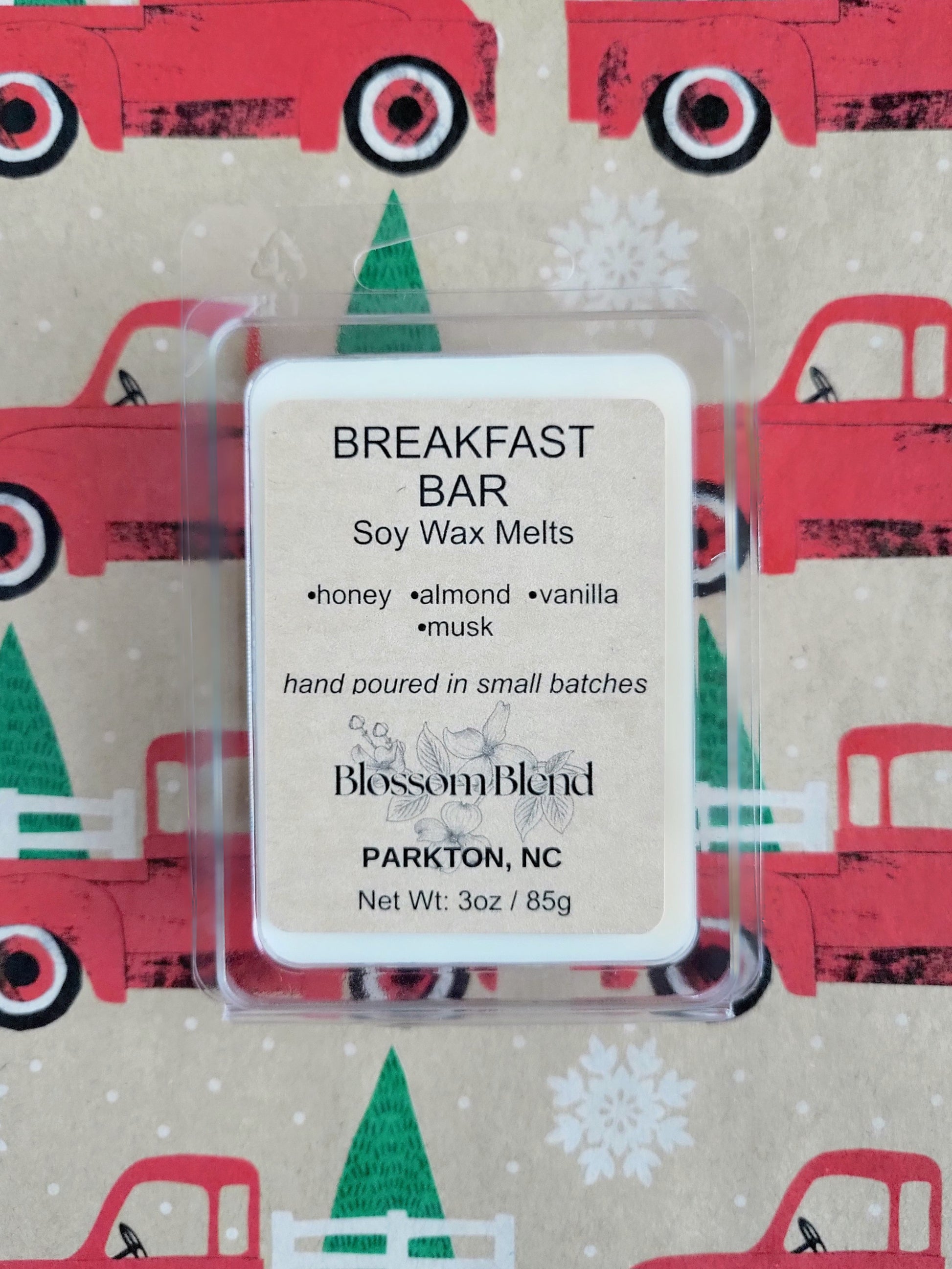 Soy wax melts packaging with 'Breakfast Bar' label on a festive background with red trucks and green trees.