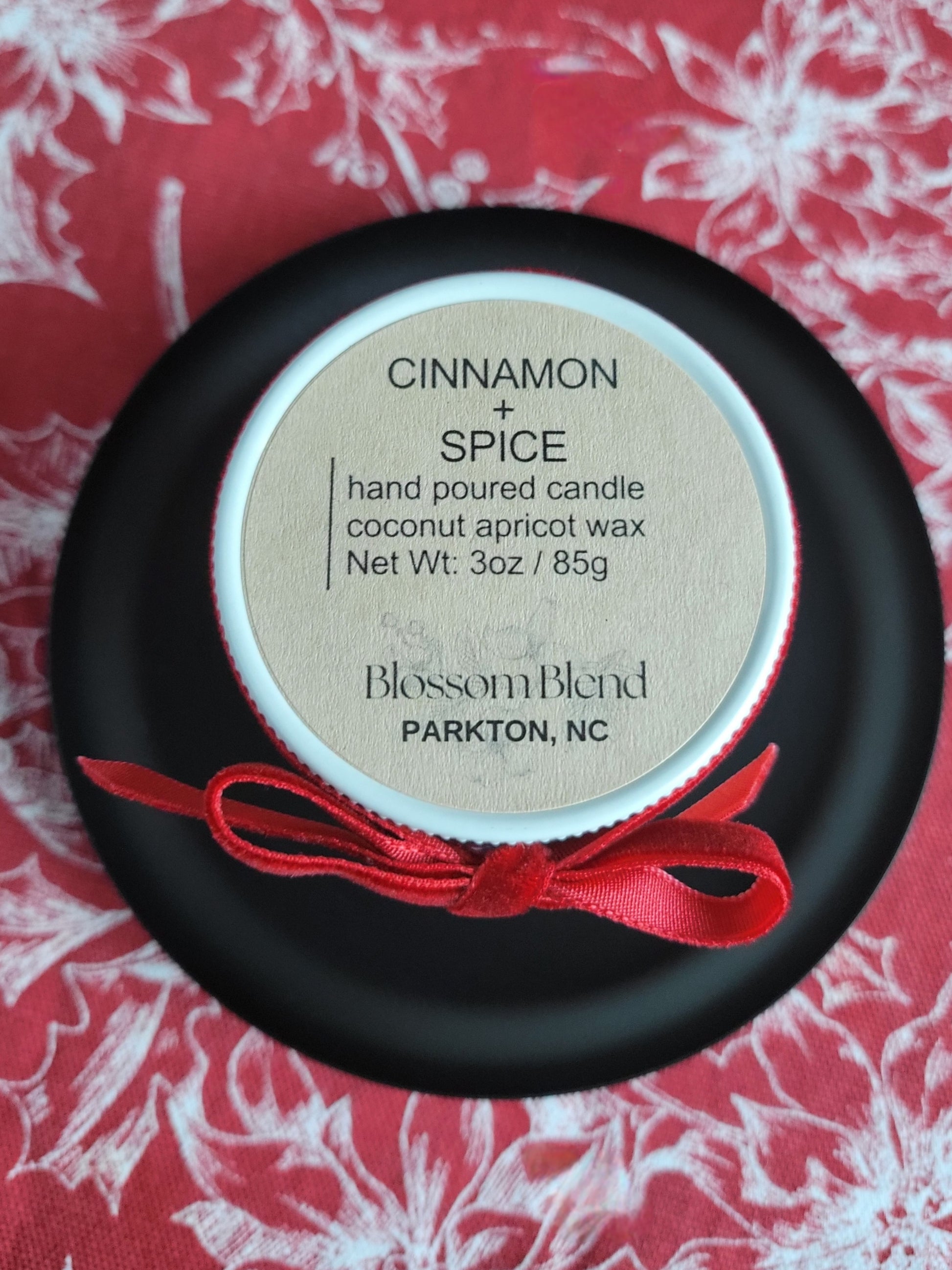 Candle container labeled 'Cinnamon + Spice' by Blossom Blend on a red floral background