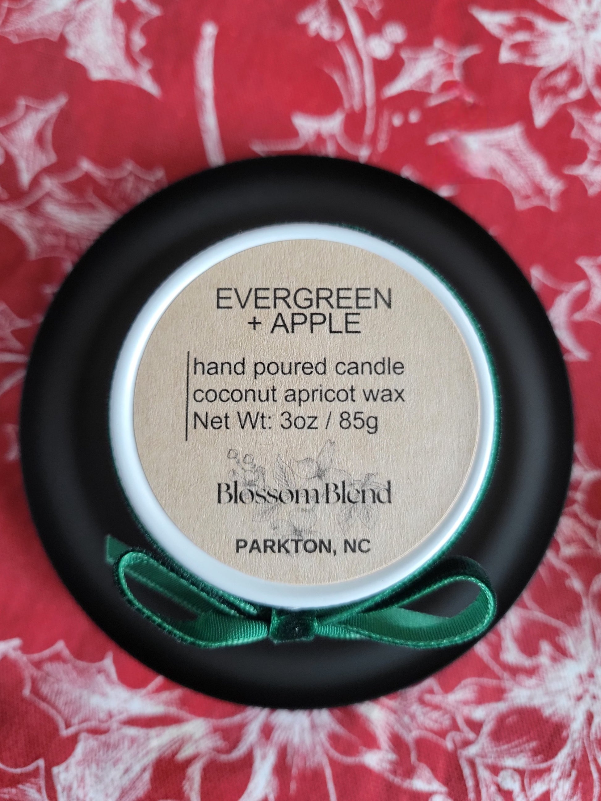 Hand poured candle labeled 'Evergreen + Apple' by Blossom Blend on a red floral background