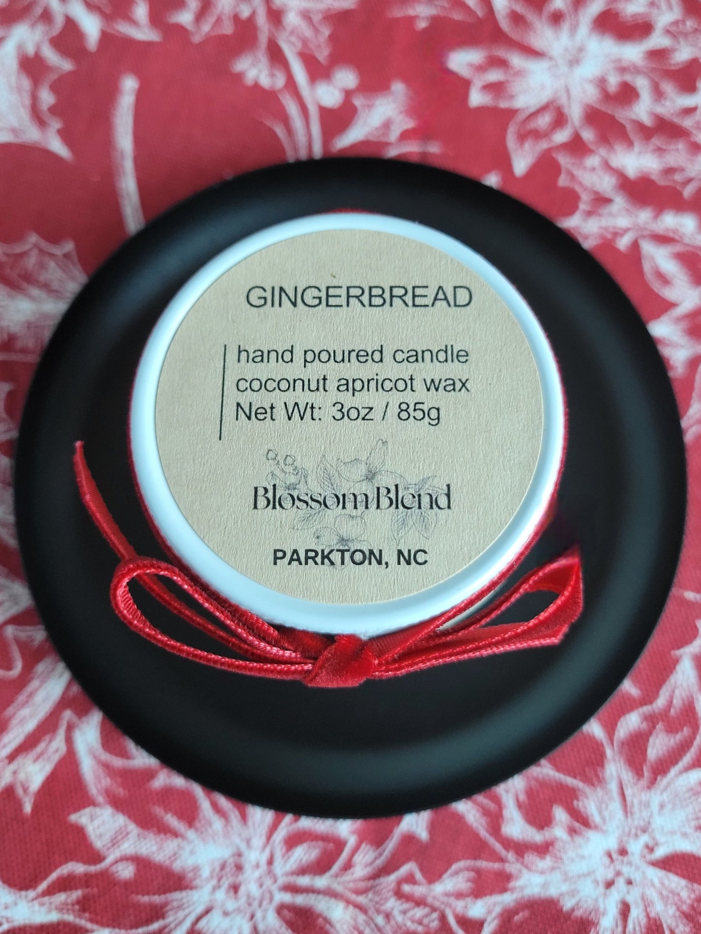 Hand poured candle labeled 'Gingerbread' by Blossom Blend on a red floral background