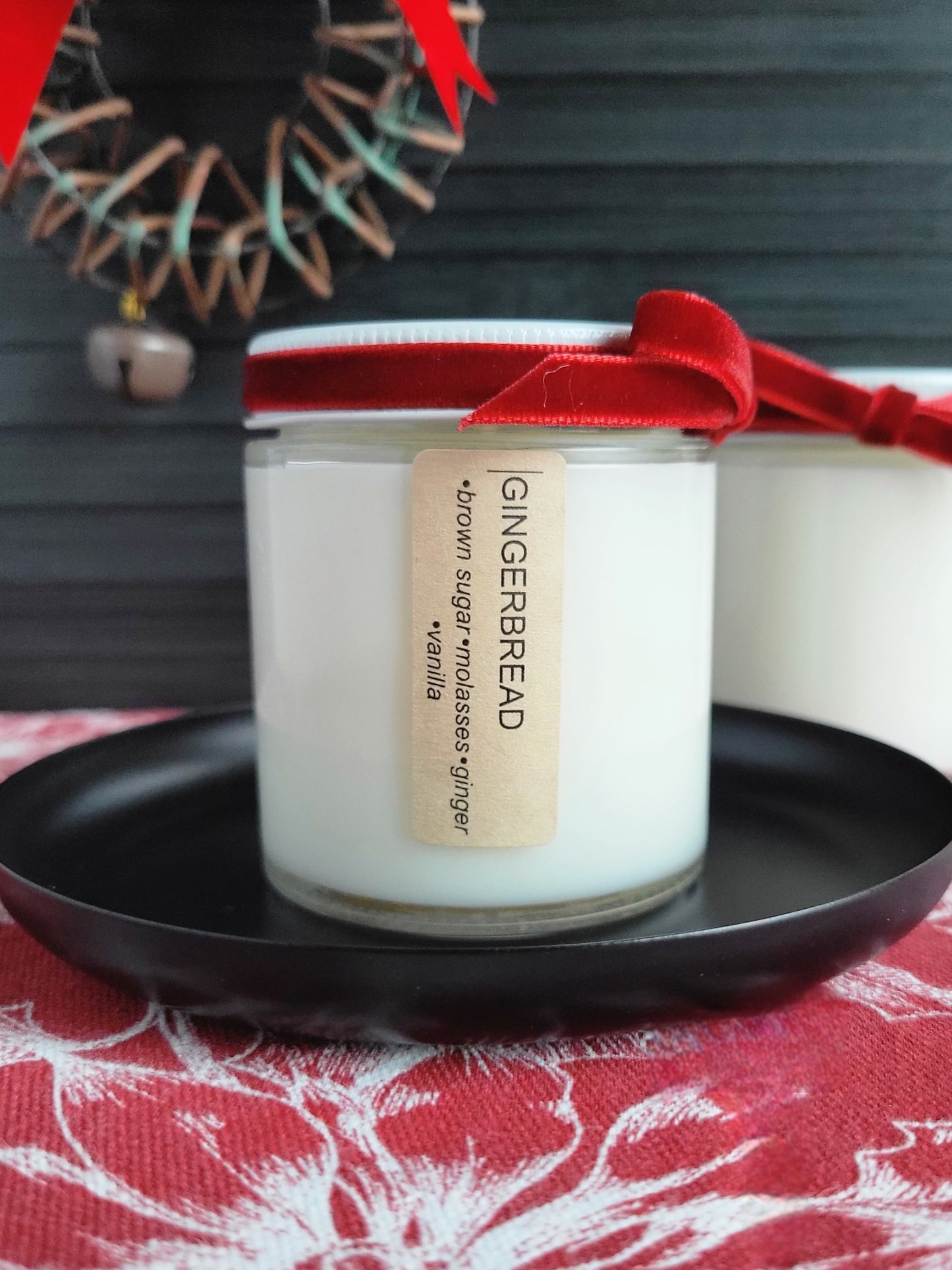 Gingerbread-scented candle with a red ribbon on a black plate against a festive background.