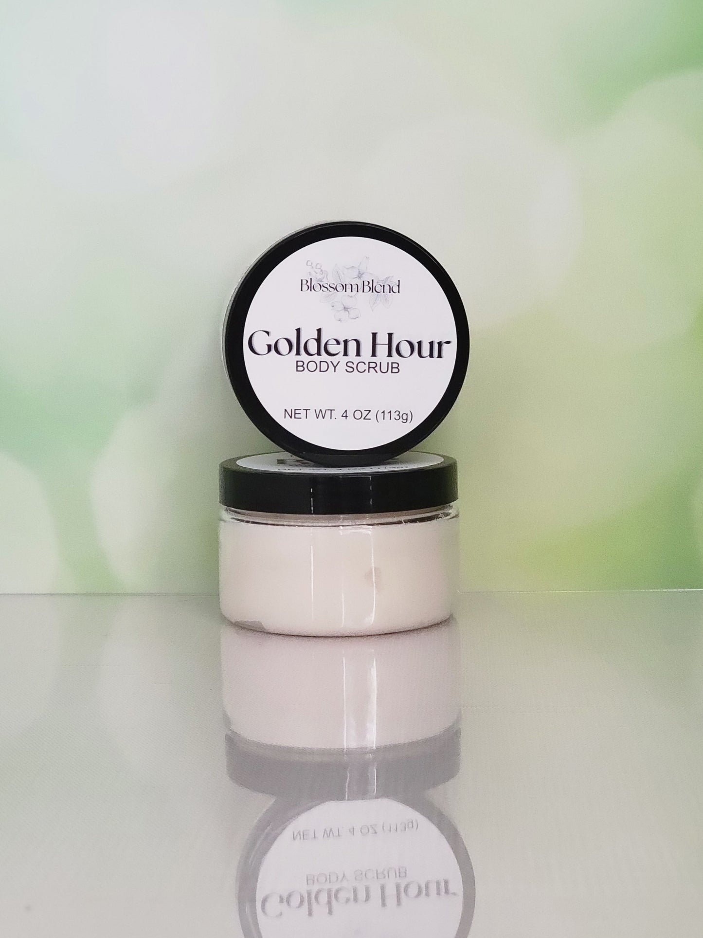 Body scrub jar with black lid and visible brand name on a light background