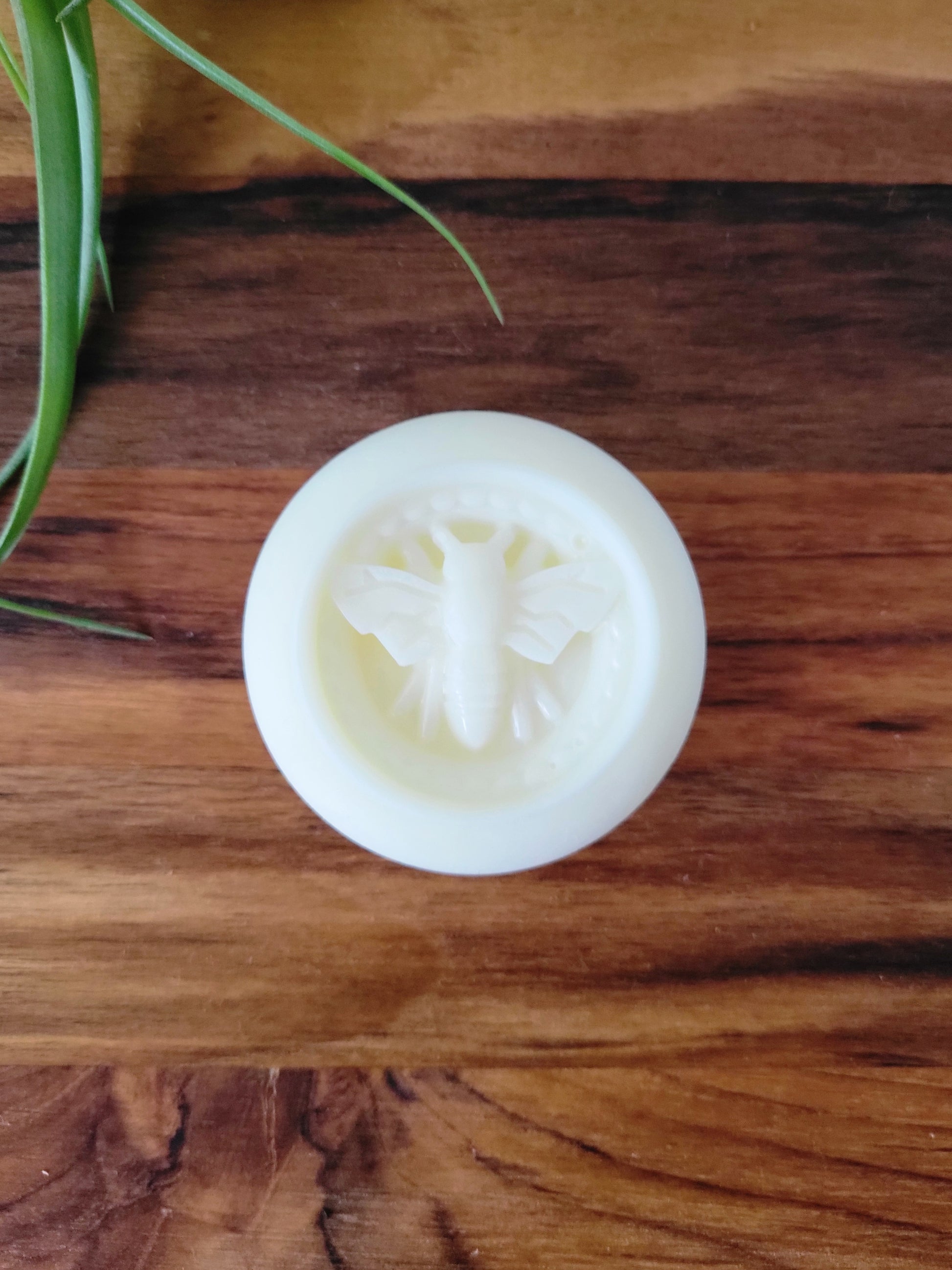 White lotion bar with a bee design on a wooden surface