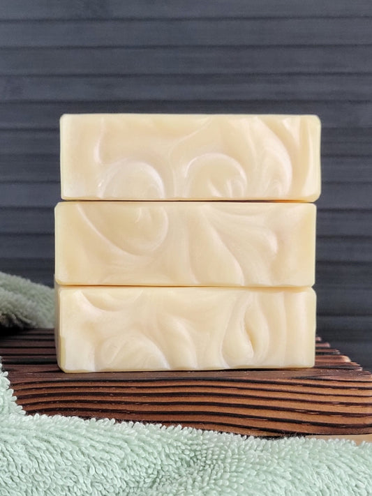 Three bars of soap with a floral pattern on a wooden block against a dark background