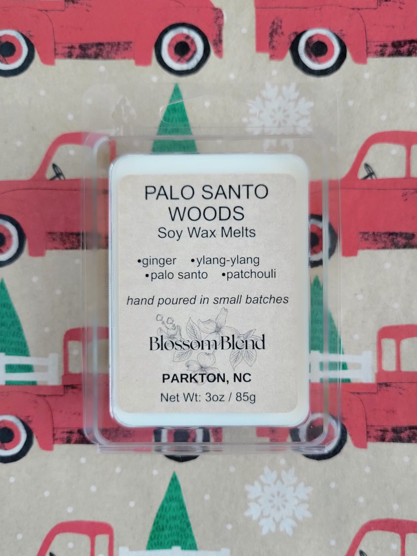 Soy wax melts packaging with 'Palo Santo Woods' label on a festive background with red trucks and green trees.