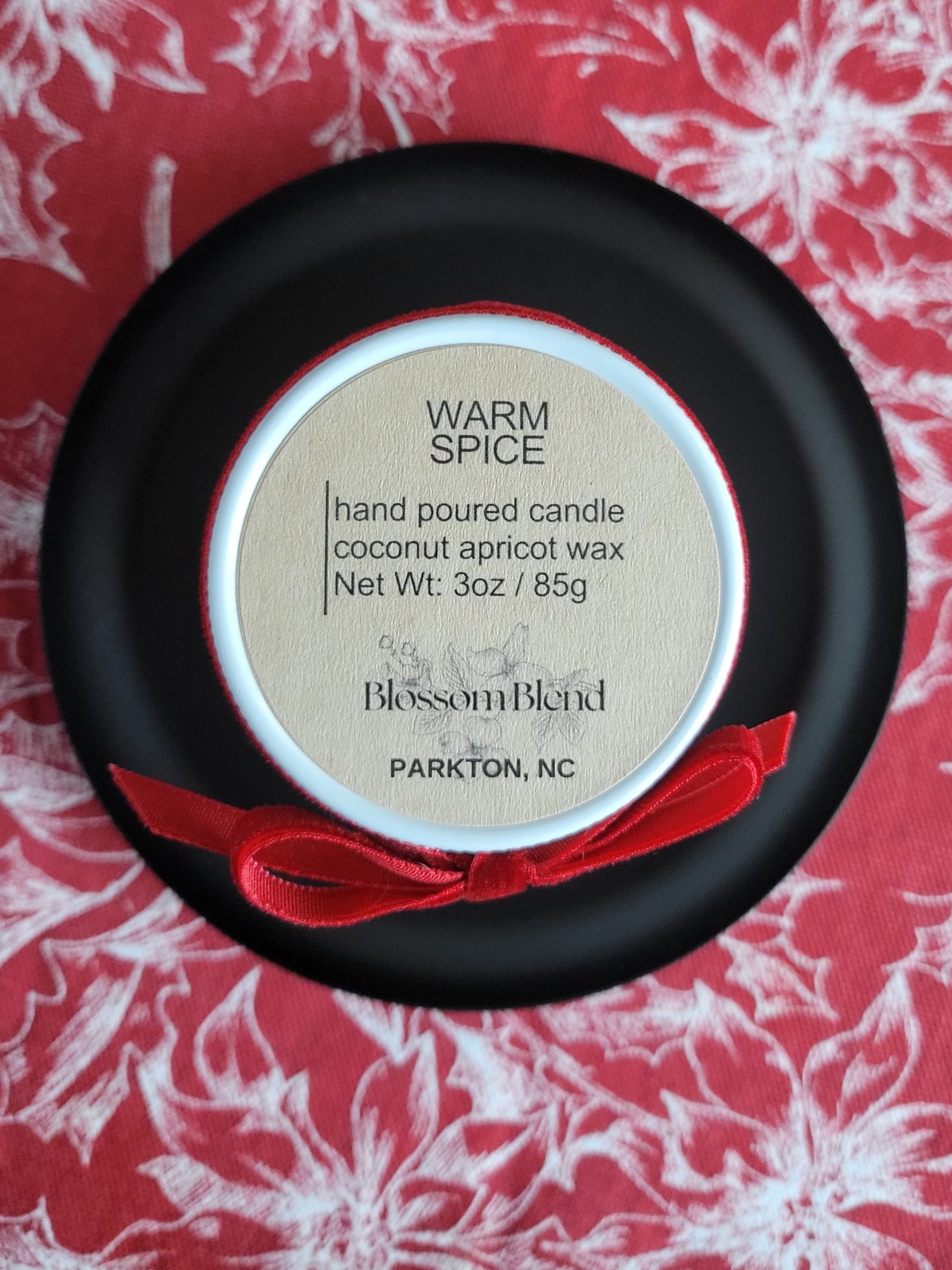 Hand poured candle in a black dish with a red ribbon on a floral patterned background