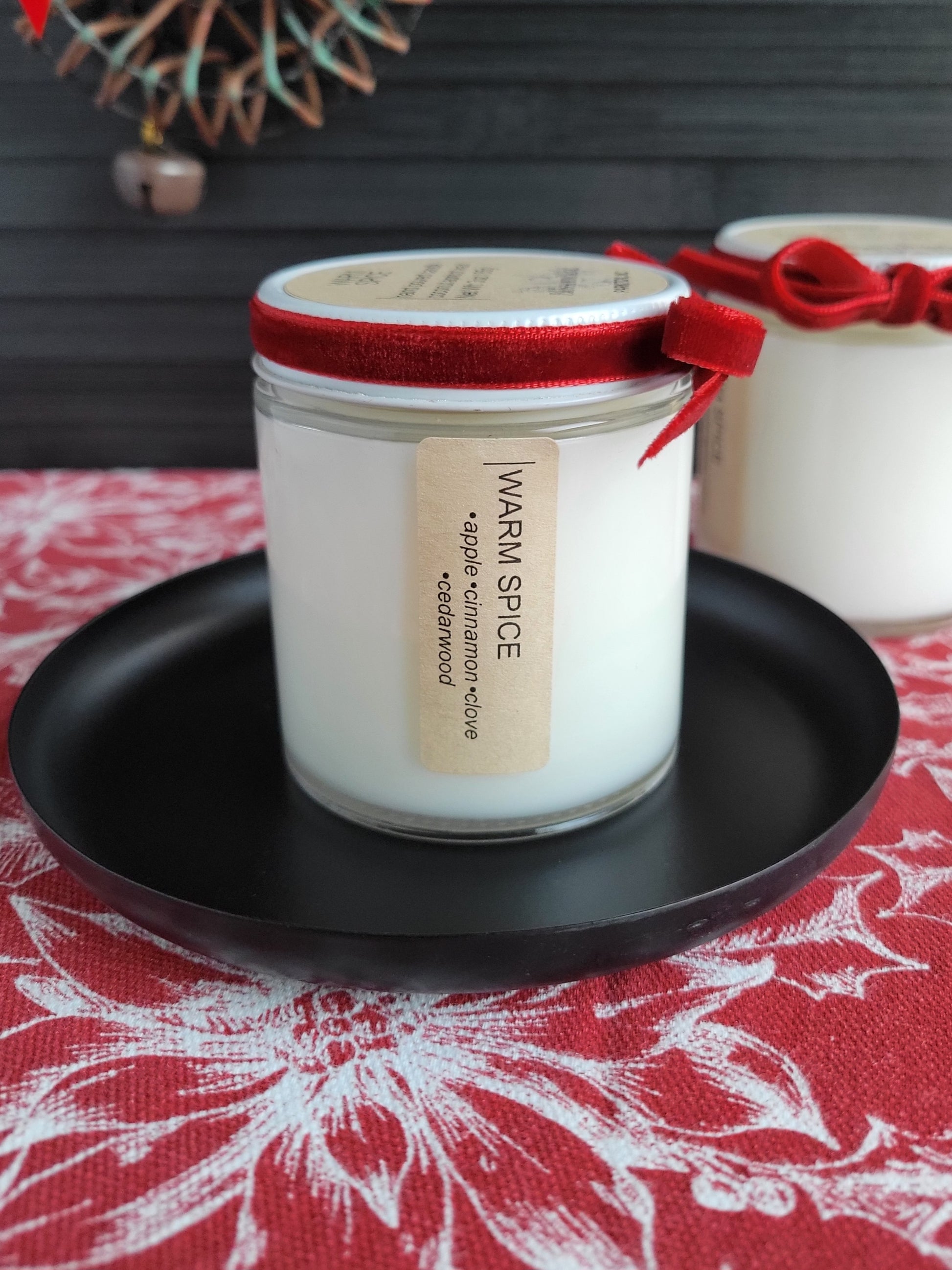 Candle in a glass jar with a red lid on a black plate, set against a decorative background.