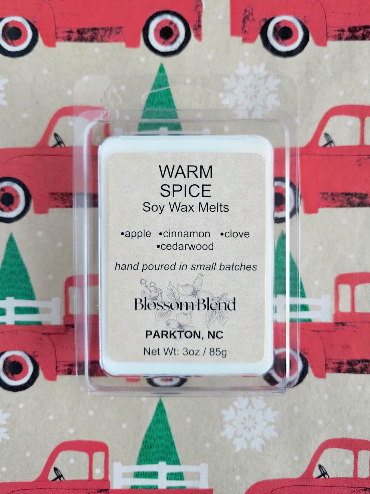Soy wax melts packaging with 'Warm Spice' description on a festive background with red trucks and green trees.