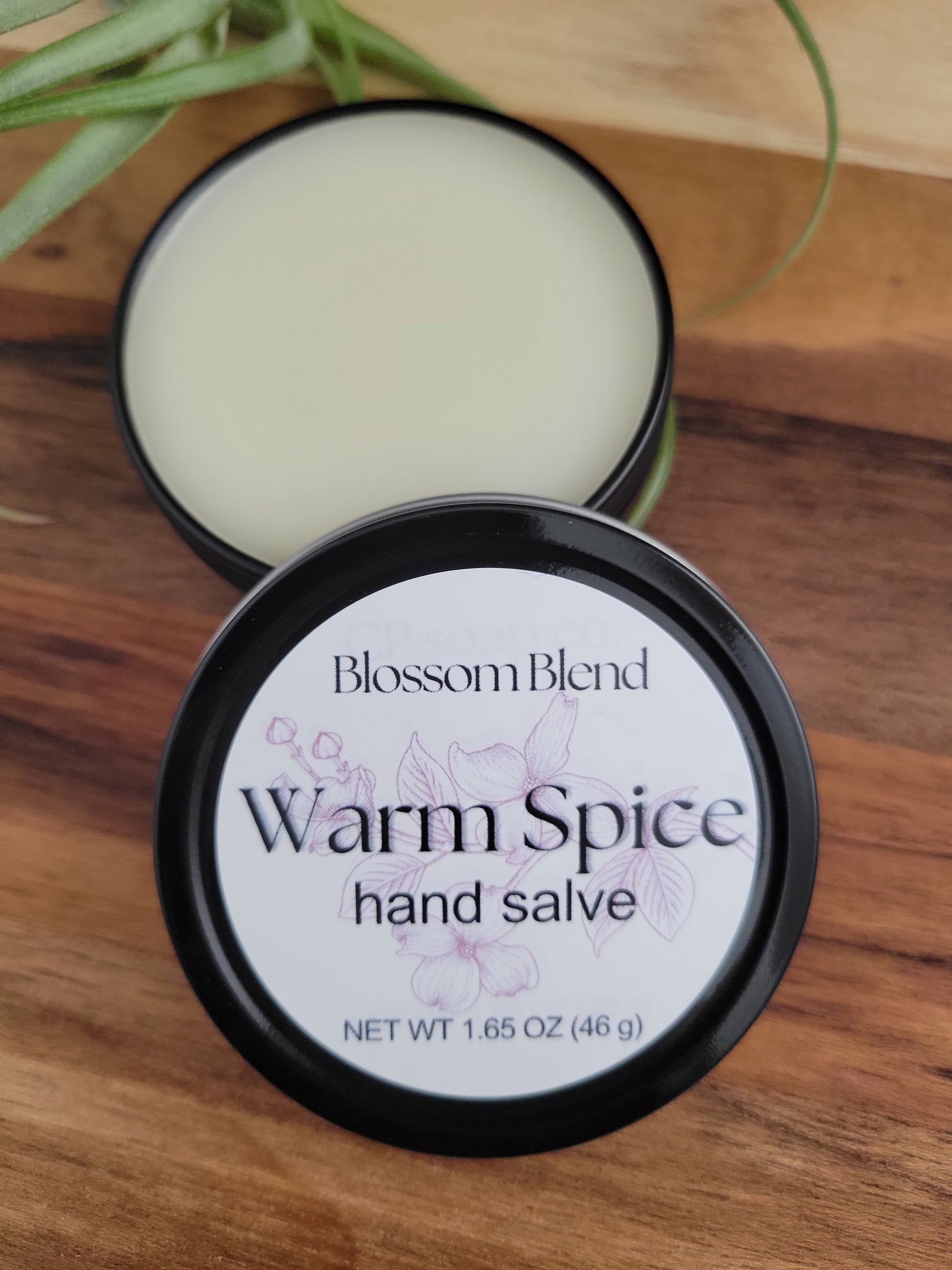 Balm container labeled 'Warm Spice' on a wooden surface with a plant in the corner.