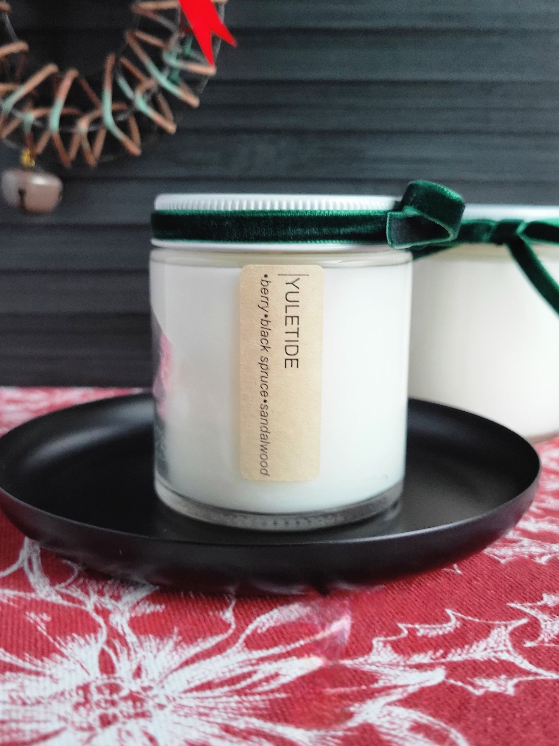 Yuletide candle in a white container with a green lid on a black plate, set against a festive background.