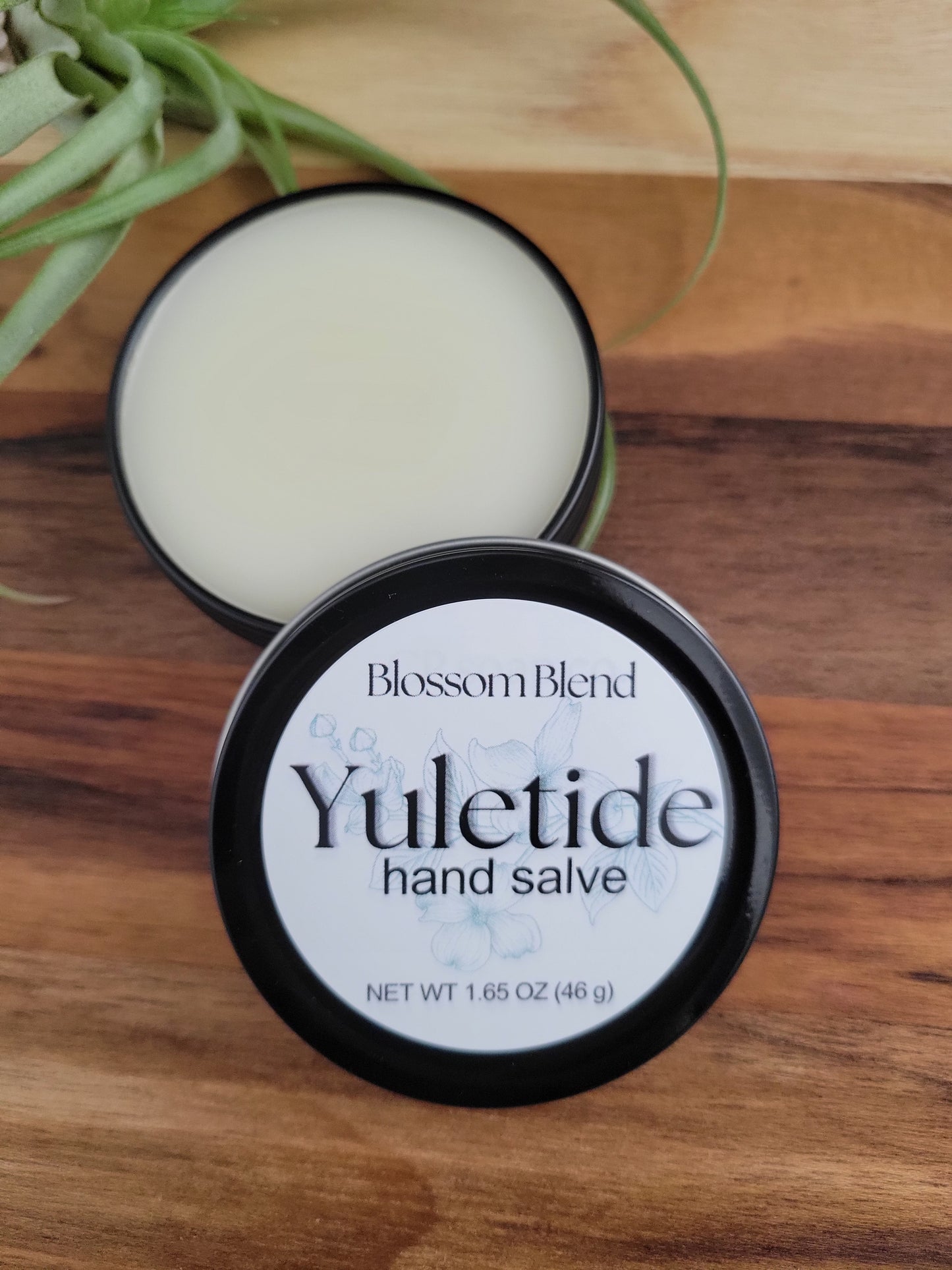 Yuletide hand salve container on a wooden surface with a plant in the corner